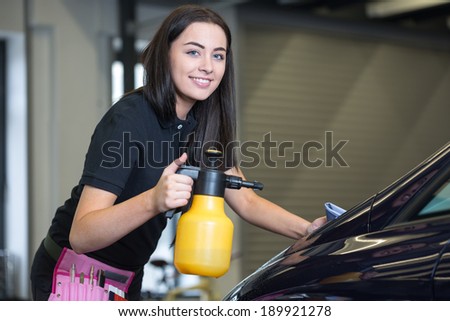 Worker cleaning car with cloth and spray bottle in garage or workshop