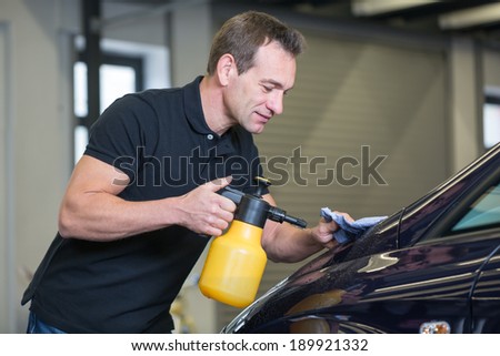 Worker cleaning car with cloth and spray bottle in garage or workshop