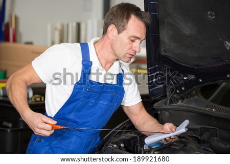 Mechanic checking oil level at a car in garage