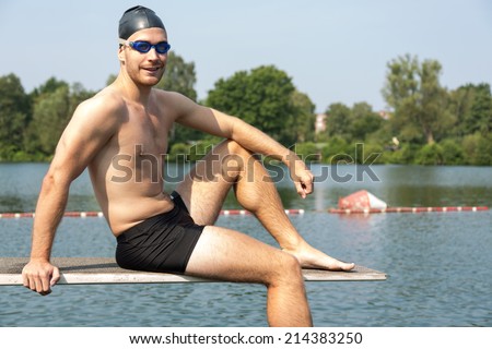 Man sitting on diving board in the sun at lake or public swimming pool