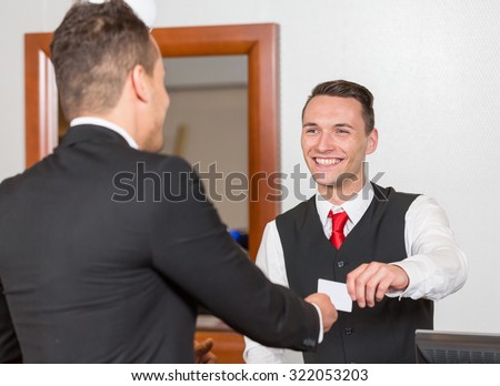 receptionist at hotel reception handing key card to guest or client