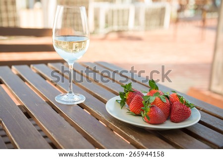 A glass of white wine and fresh strawberries on a plate on an open terrace in summer