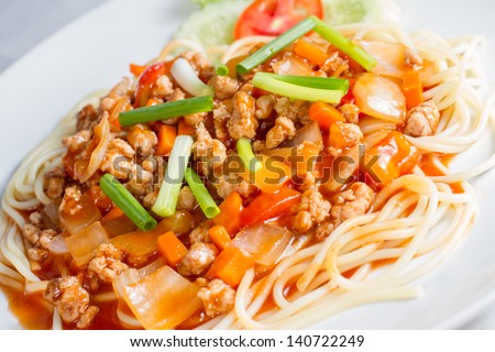 Closeup of spaghetti with meat, tomato sauce, and vegetables on white dish