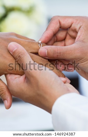 groom hand putting a wedding ring on the bride finger