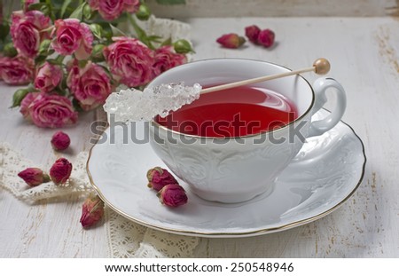 Cup of tea with dried rose buds and fresh roses on a light background