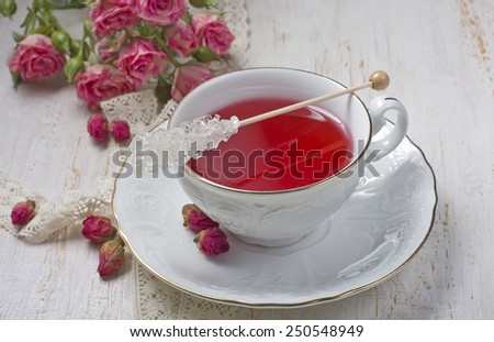 Cup of tea with dried rose buds and fresh roses on a light background