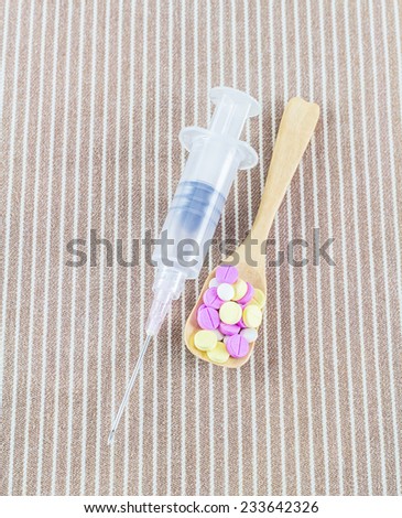 Syringe with needle and different pills in wooden spoon - health care system