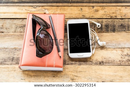 Notebook,sunglasses,smart phone and earphone on wooden table background