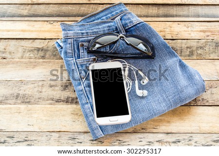 White earphone,sunglasses,smart phone and blue jeans on wooden table background