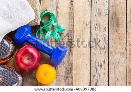 Blue dumbbell, white towel, measuring tape and red apple on wooden table. Fitness concept