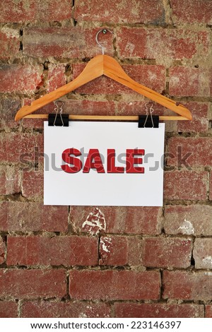 Sale sign hanging on coat hanger against rustic brick wall