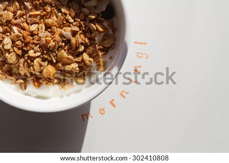 The word Morning stamped next to a bowl of muesli and yogurt with hard shadow to convey outdoor dining