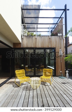 Pair of yellow cane outdoor chairs on wooden deck in contemporary courtyard