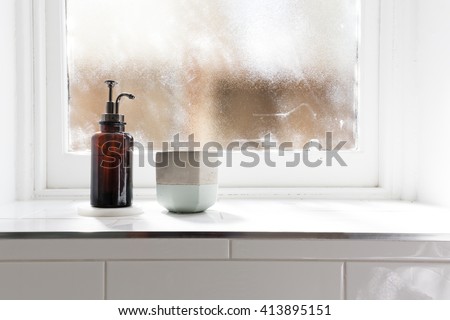Bathroom soap dispenser and pot on window ledge with background of negative space horizontal
