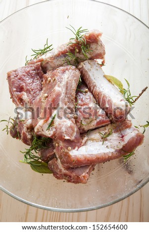 Raw pork chops in a glass bowl with fresh herbs and olive oil