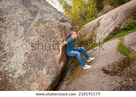 Man with backpack pushing a huge stone