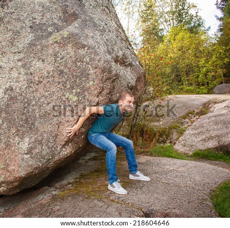 Man with backpack pushing a huge stone