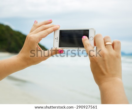 Woman hands showing a blank smart phone screen display on the beach with the sea in the background