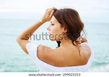 Relaxing beach woman enjoying the summer sun in white dress. Glamorous girl with gold tattoo on the hand.