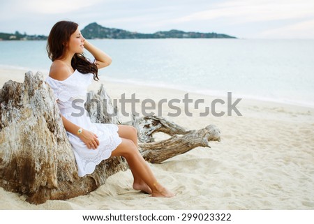 Relaxing beach woman enjoying the summer sun in white dress. Glamorous girl with gold tattoo on the hand.