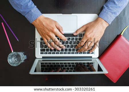 Cropped image of a young man working on his laptop at home, top view of business man hands busy using laptop at office desk