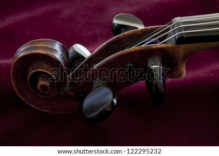 A low key image of a violin scroll resting on burgandy velvet.