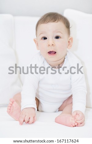 An adorable, happy baby looking at camera on white pillows