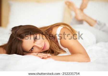 Happy delicate woman lying on bed with crossed legs looking into camera in bedroom