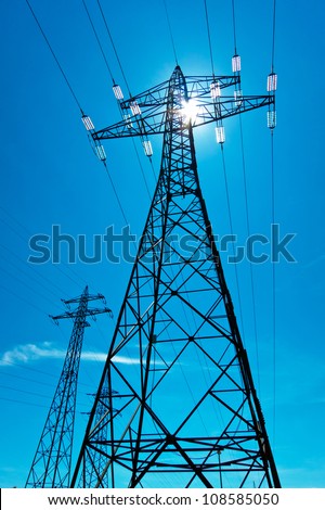 the utility pole of a high voltage line with the sun and blue sky. energy supply from power line.