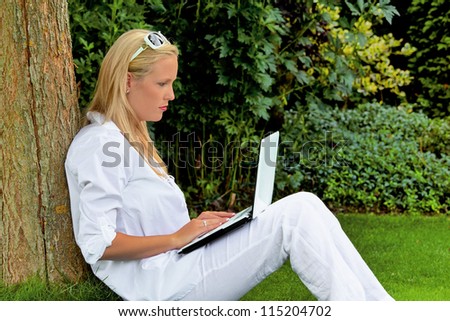 a young woman sitting with a laptop computer in the garden and surfs the internet. wi-fi in the park
