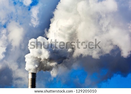 the smoking chimneys of a factory against a blue sky. smoke rises from chimneys white