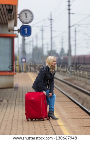 a young woman with luggage waiting on the platform of a railway station for their train. train delays