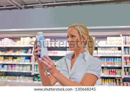 a young woman buys milk at the supermarket. stands in front of the refrigerated section.
