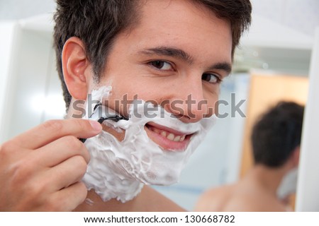 young man shaving with razor and shaving cream in bathroom