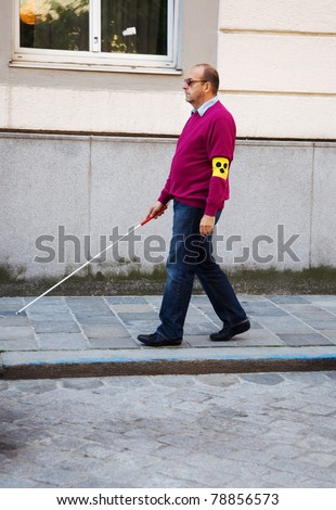A blind man walks with a cane on a street