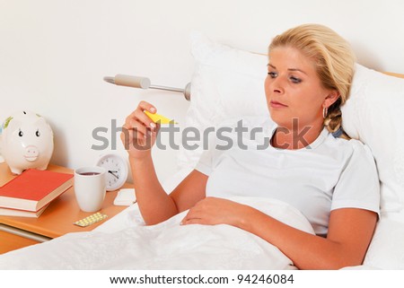 a woman is sick in bed and has a fever thermometer.