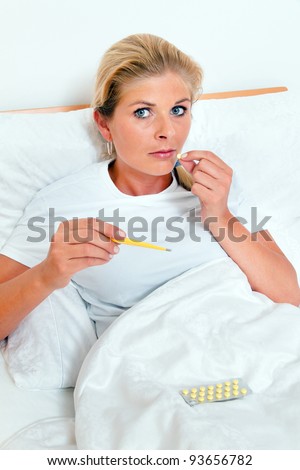 a woman is sick in bed and has a fever thermometer.