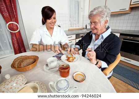 a geriatric nurse helps elderly woman at breakfast