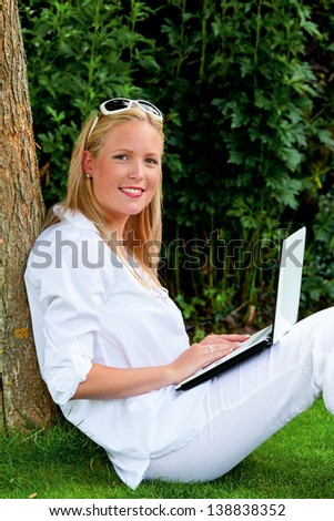a young woman sitting with a laptop computer in the garden and surfs the internet. wi-fi in the park