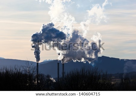 the smoking chimneys of a factory against a blue sky. white smoke rises from chimneys on