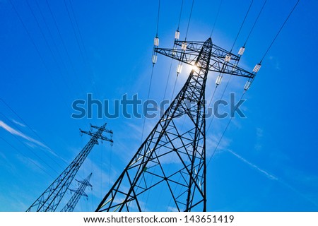 a power mast of a high voltage transmission line against blue sky with sun