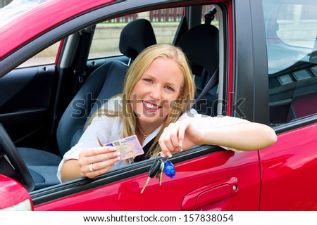 a young woman sitting in her car and proudly shows her license after passing the driving test.