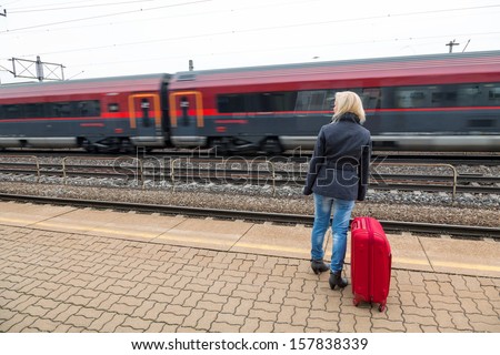 a young woman with suitcase waiting on the platform of a railway station on their train. train delays
