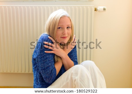 a young woman sits in front of a radiator in winter. room temperature is too low.