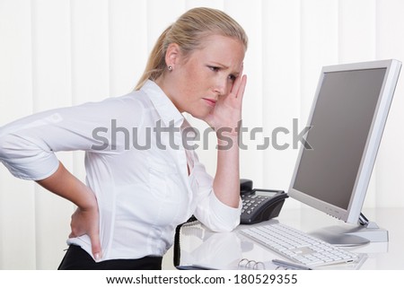 a woman sitting in office front of her computer and has back pain.