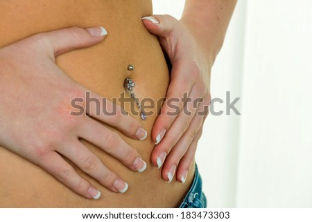 a woman has abdominal pain or stomach pain. hands in a heart shape around navel piercing.
