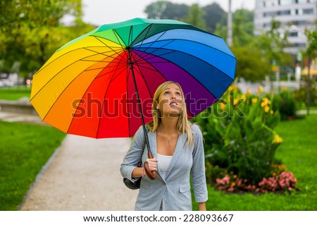 a young woman walks with a colorful umbrella in hand walking in the rain.