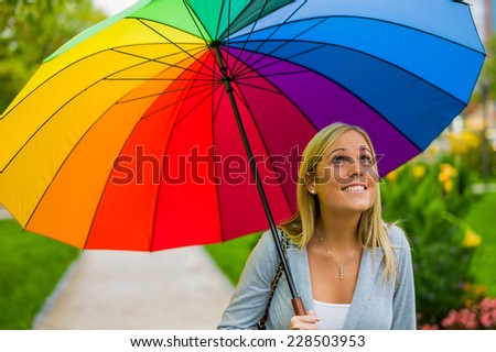 a young woman walks with a colorful umbrella in hand walking in the rain.