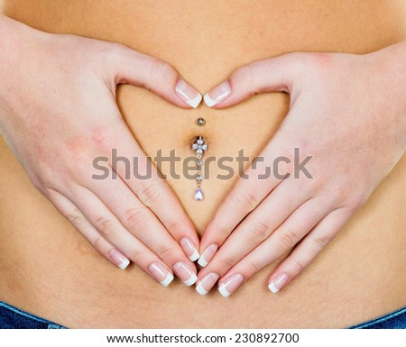 a woman has abdominal pain or stomach pain. hands in heart shape around navel piercing.