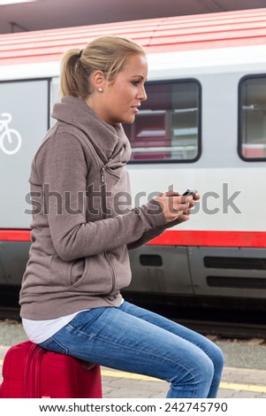 a young woman waiting for a train and writes with her cell phone a sms
